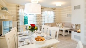 Uma área de refeições com uma mesa posta para dois, uma cesta de croissants e um vaso com flores.