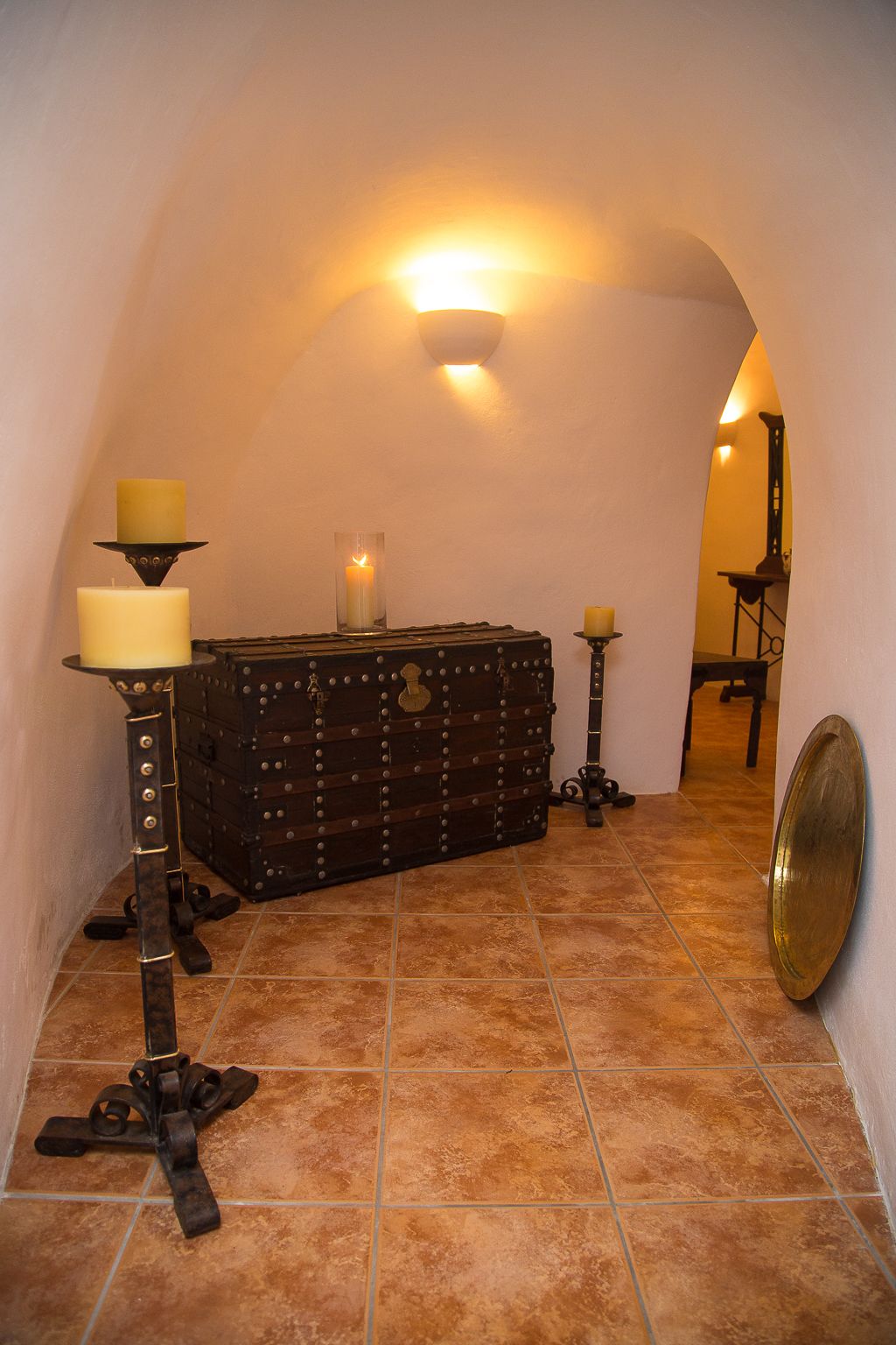 A narrow, arched hallway with a rustic chest of drawers, two candles, and a wall-mounted light fixture.