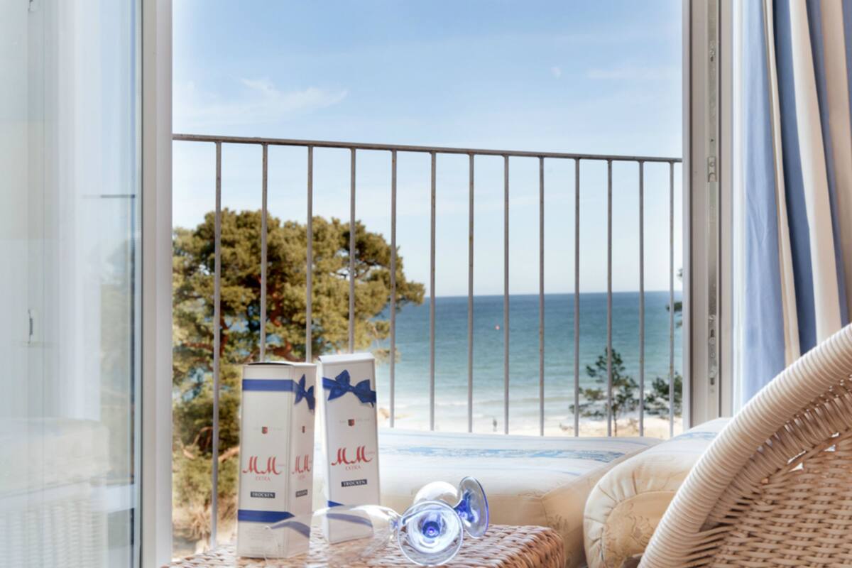 Un balcón con vista al mar, mobiliario de mimbre y dos cajas con un lazo azul.