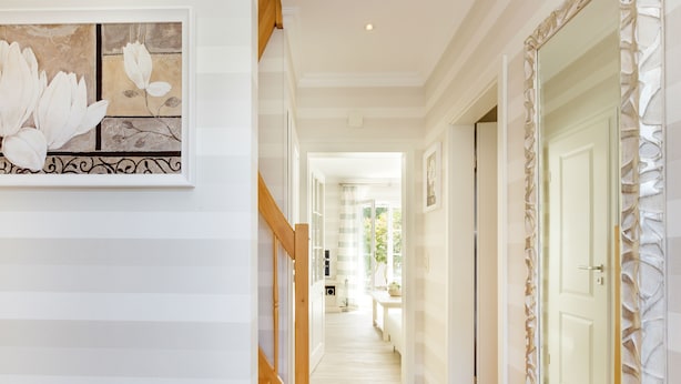 A hallway with a wooden floor, white walls, and a framed floral artwork.