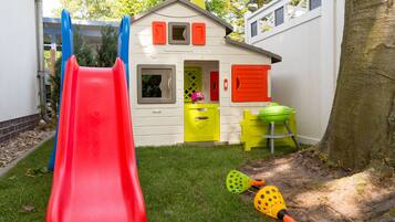 Children can play safely in this outdoor play area featuring a colorful playhouse with a slide.