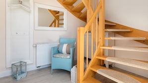Una escalera con escalones de madera y barandilla, un radiador blanco, una silla azul con cojín y una puerta blanca con un espejo encima.