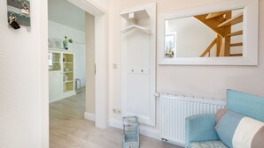 Una habitación con una puerta blanca, un radiador blanco, un sofá de mimbre azul y un espejo en la pared.