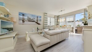 Una sala de estar moderna con un sofá color beige, un televisor de pantalla plana y un comedor con mesa y sillas.