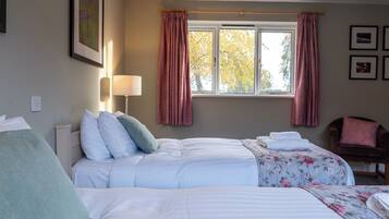 Quarto de hotel com duas camas, uma janela com cortinas, uma cadeira e quadros na parede.