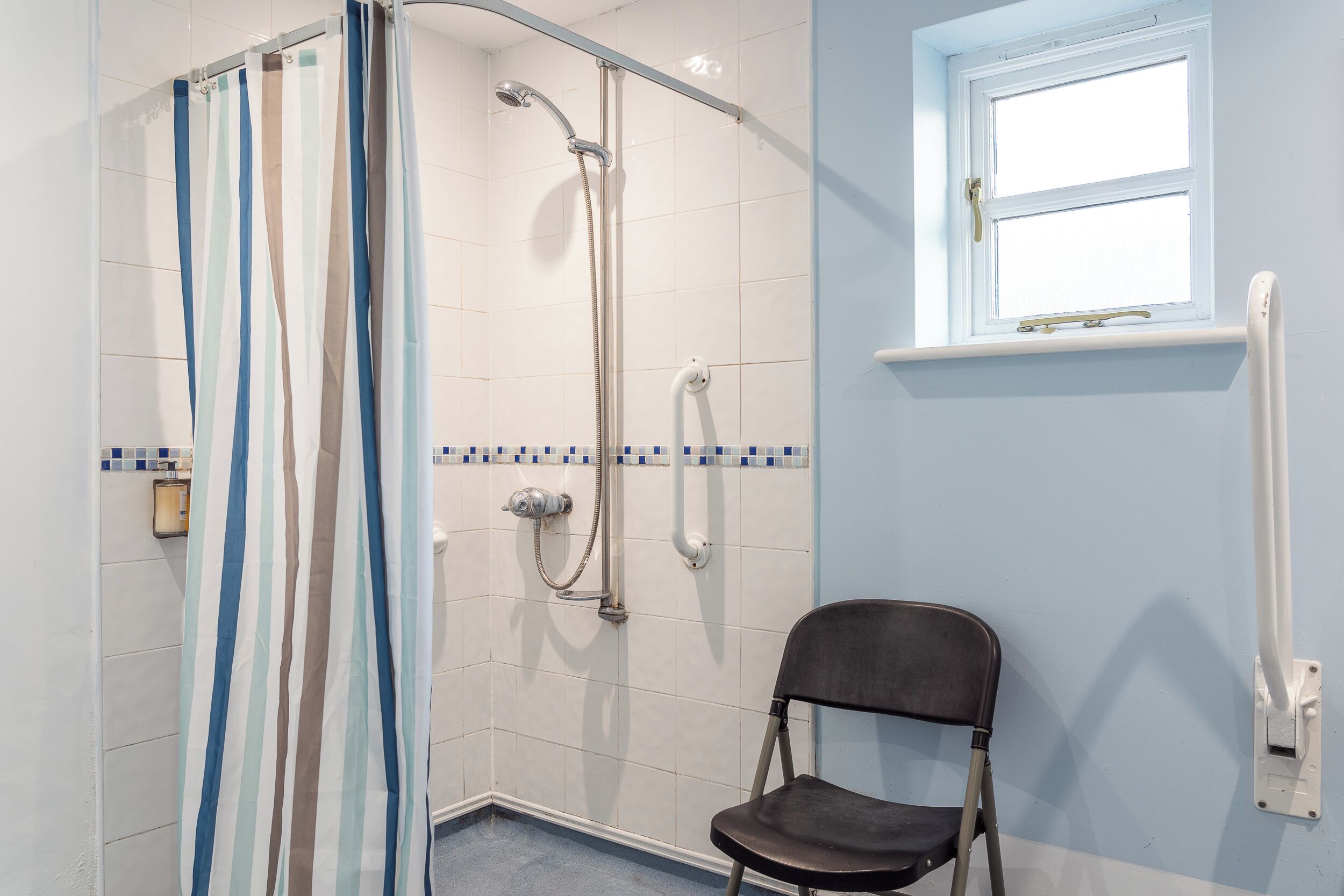 A shower area with a striped curtain, a handheld showerhead, and a chair.