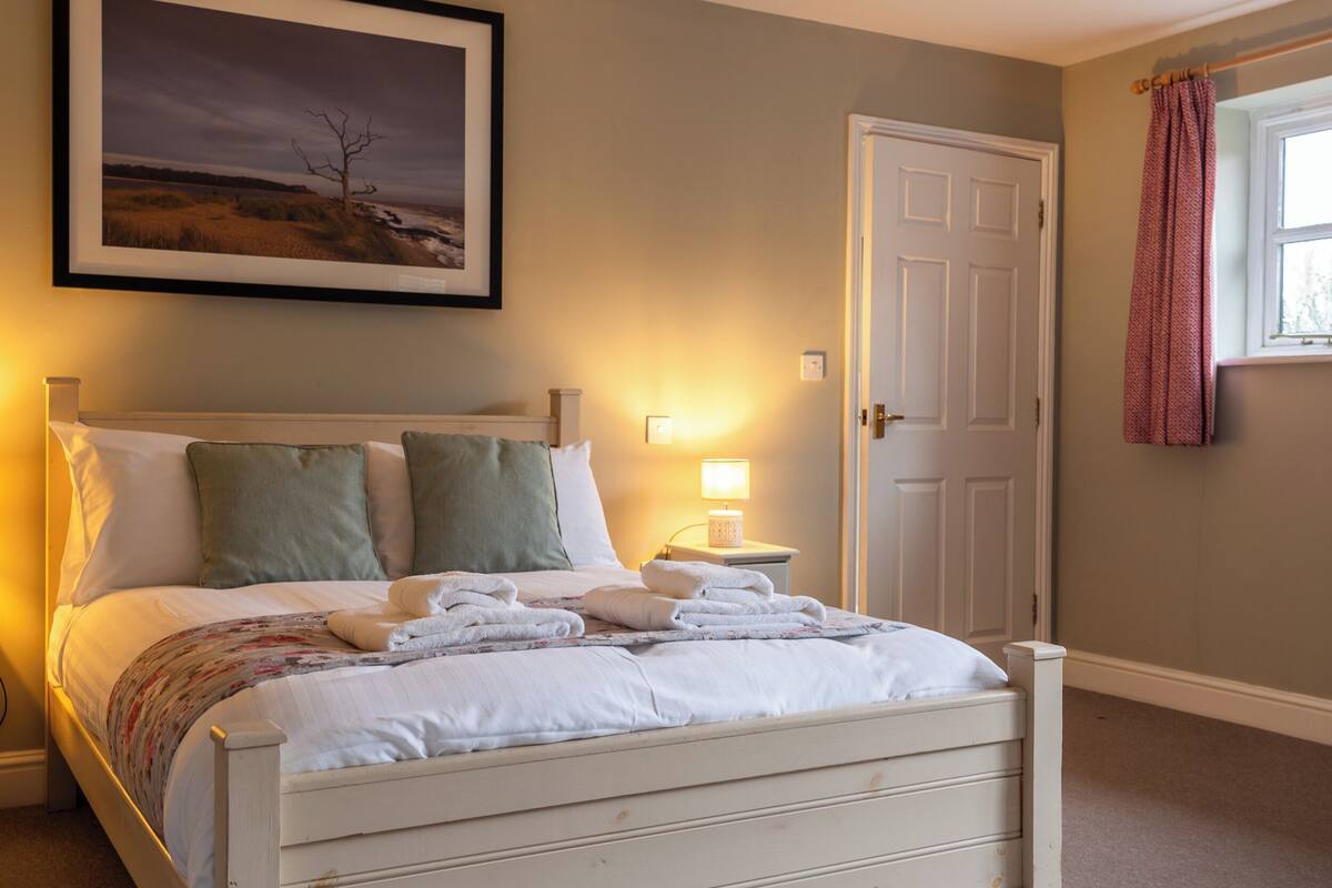 A neatly made bed with pillows, a bedside lamp, and a framed landscape picture on the wall.