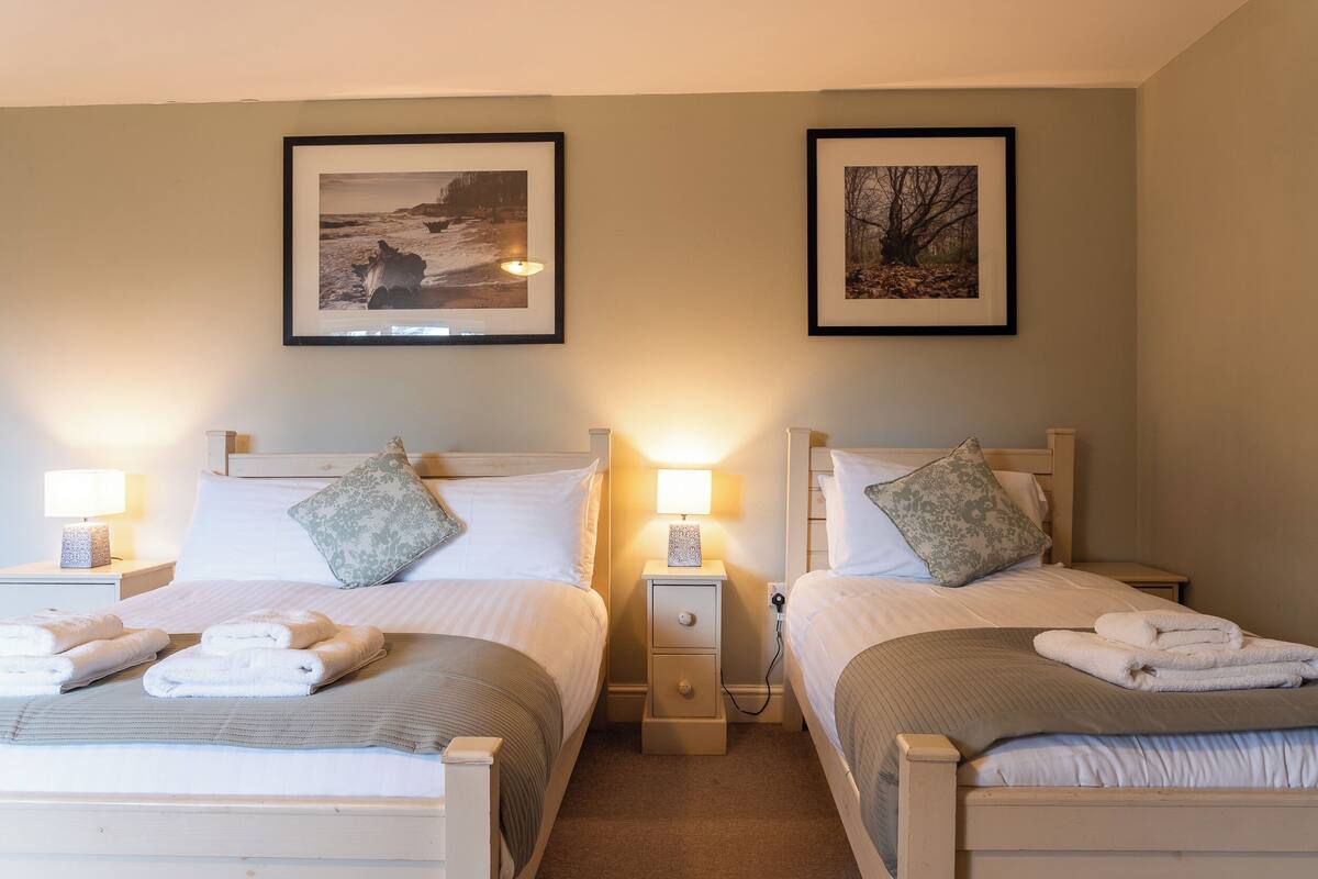 A twin bedroom with two beds, each with a pillow, a bedside table with a lamp, and a framed picture on the wall.