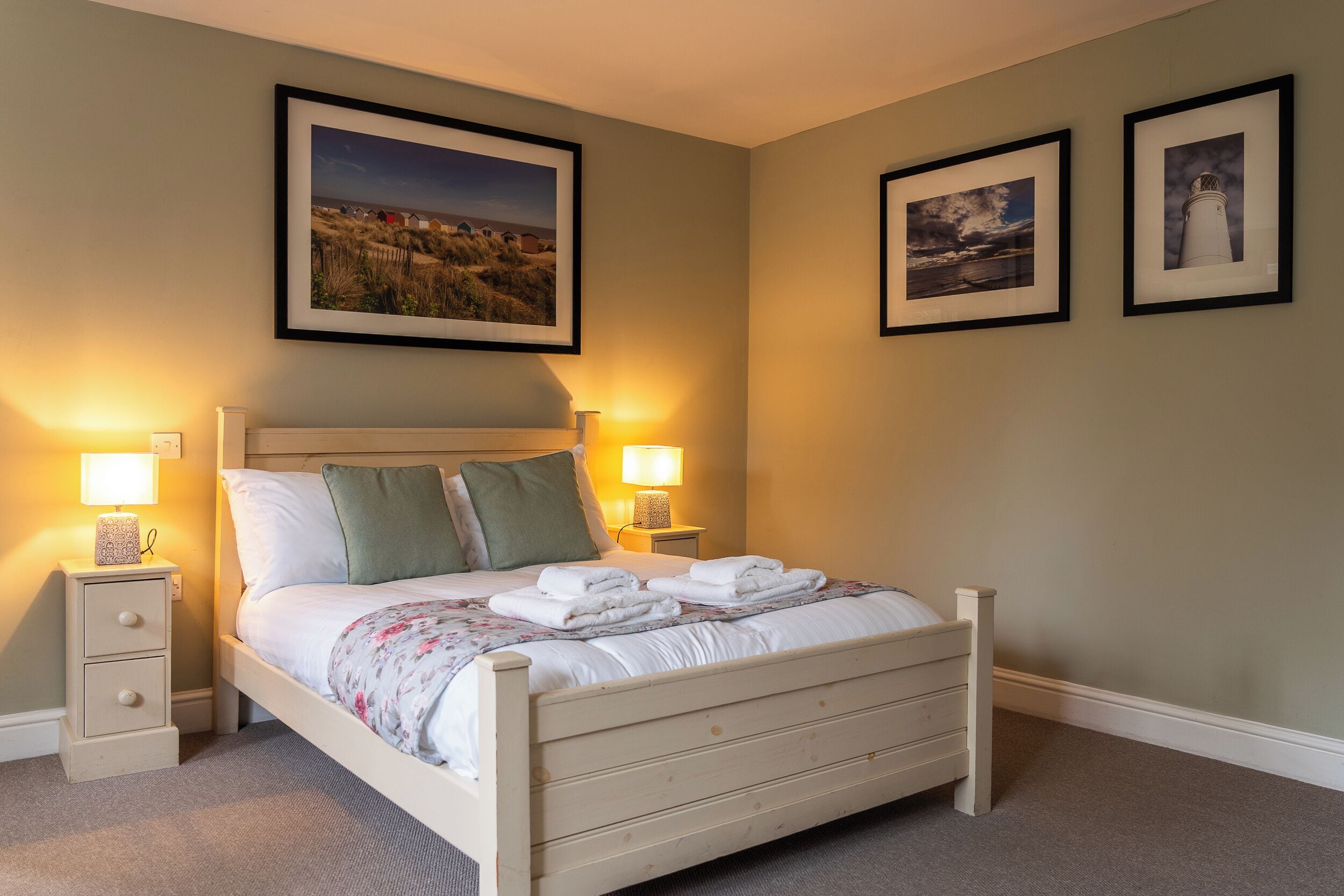 A neatly made bed with pillows and a blanket, two bedside tables with lamps, and framed pictures on the wall.