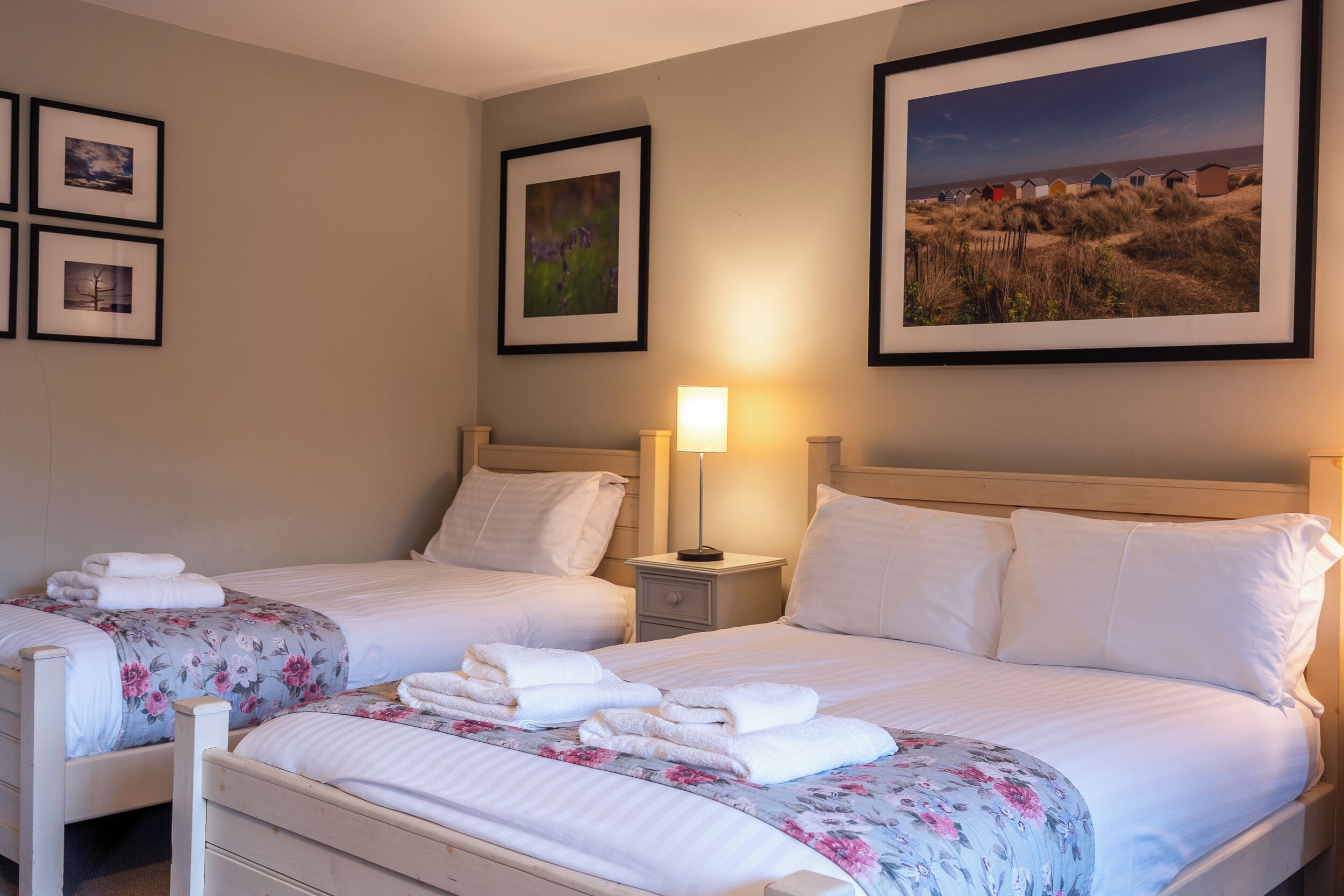 Ein Hotelzimmer mit zwei Betten, einem Nachttisch mit Lampe und gerahmten Bildern an der Wand.