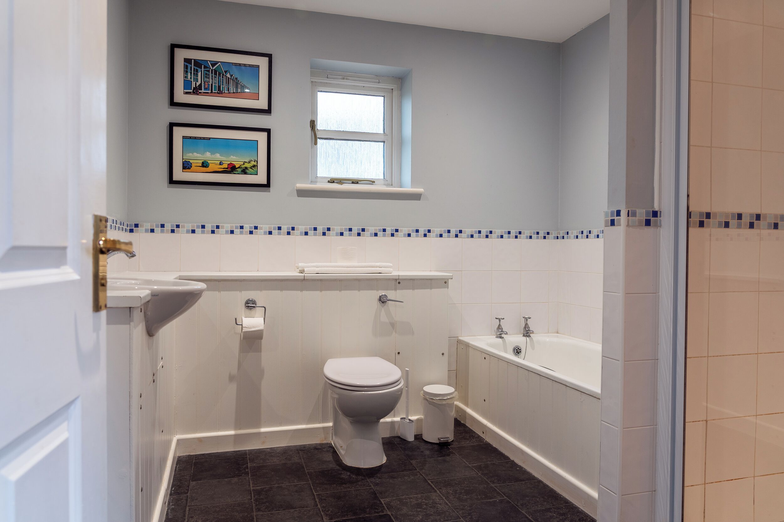 A bathroom with a toilet, sink, and bathtub. There are two framed pictures on the wall.