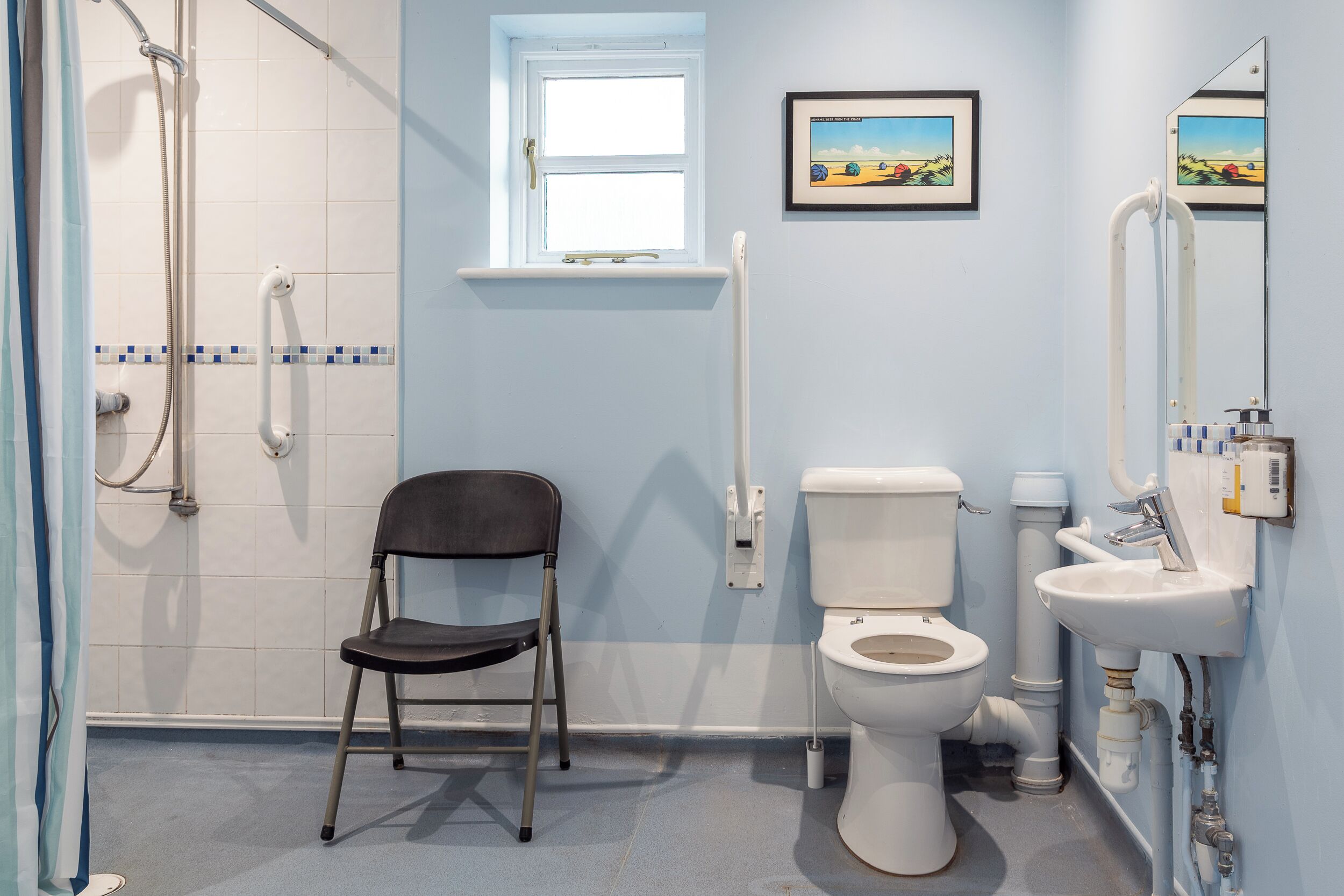 Un baño con ducha, inodoro y lavamanos, una silla y una ventana con vistas al paisaje.