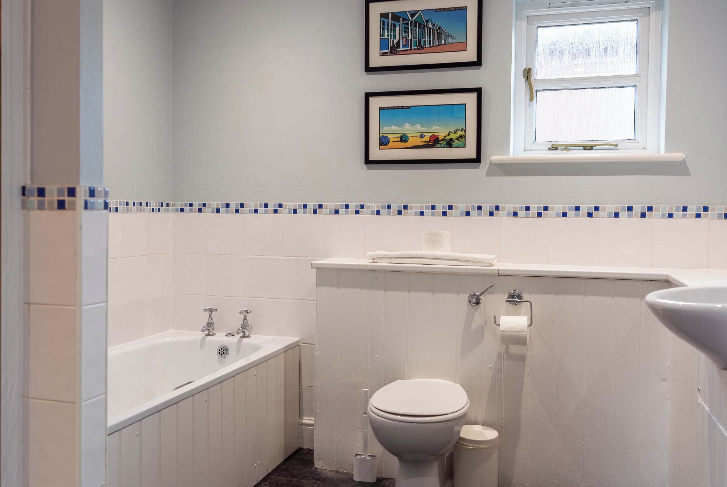 Un baño con bañera, inodoro y lavamanos. Hay dos cuadros en la pared.