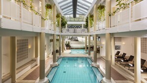 Una piscina interior con una isla central, rodeada de zonas de descanso y un techo de cristal.