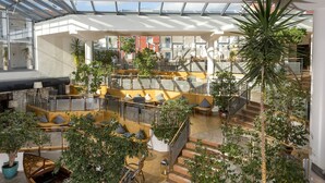 Un amplio atrio interior con varias zonas de descanso, una escalera y una diversidad de plantas en macetas.