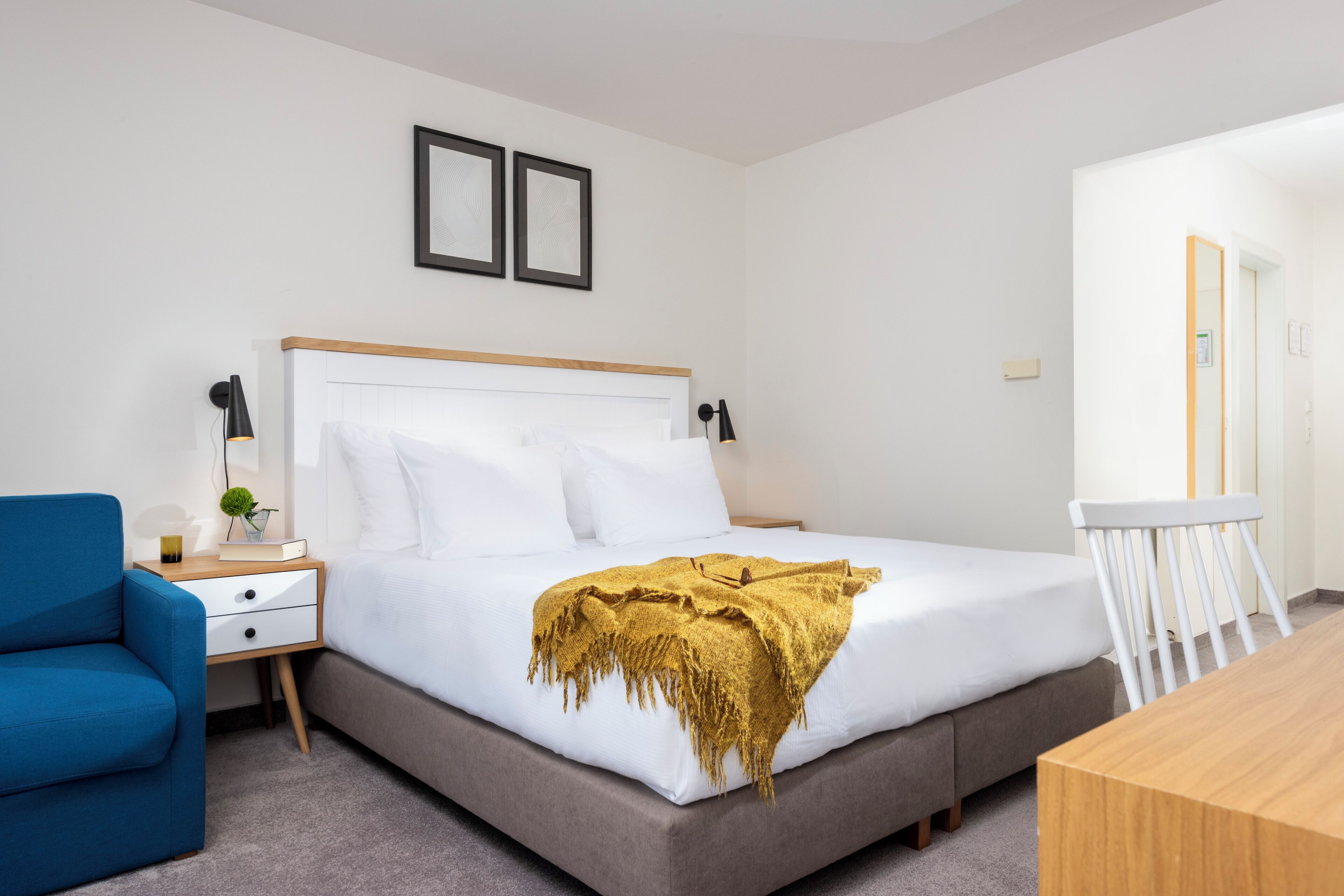 Une chambre à coucher bien rangée, avec un lit, une table de chevet, une lampe, une chaise et une petite table avec un miroir.