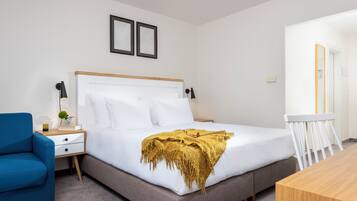 Ein ordentlich eingerichtetes Schlafzimmer mit Bett, Nachttisch, Lampe, Sessel und einem kleinen Tisch mit Spiegel.