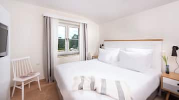 Una habitación de hotel con una cama grande, una mesita de noche con lámpara, una silla y un televisor en la pared.