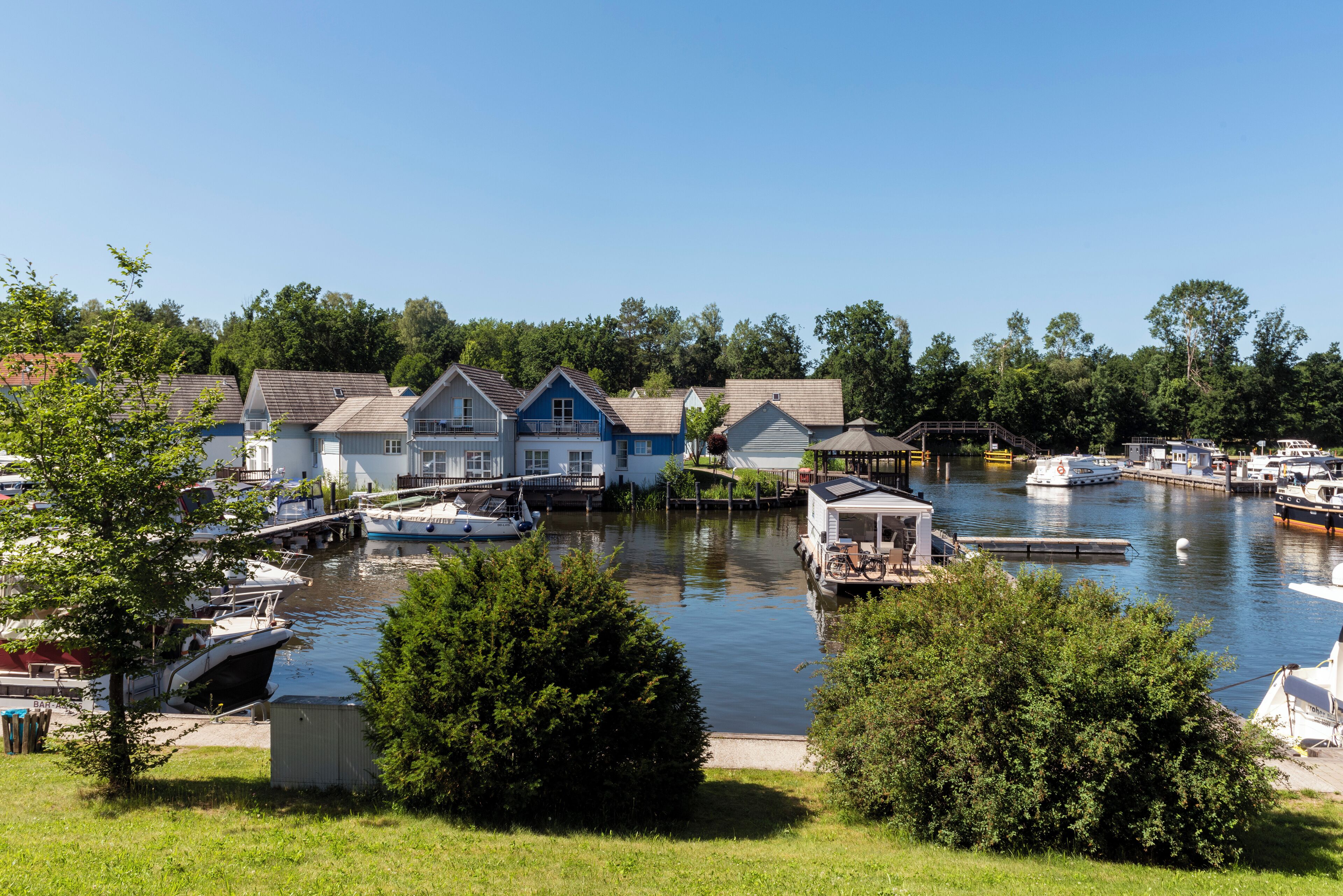 A marina with boats docked, a small boat house, and a building with a blue roof.