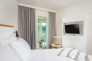 A hotel room with a bed, a television mounted on the wall, a chair with a yellow hat, and a view of the outside balcony through a glass door. - Sunday Resort Marina Wolfsbruch (Rheinsberg)