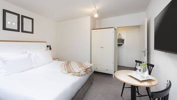 Een hotelkamer met een bed, nachtkastje, stoel, rond tafel, kledingkast en een aan de muur bevestigde televisie.