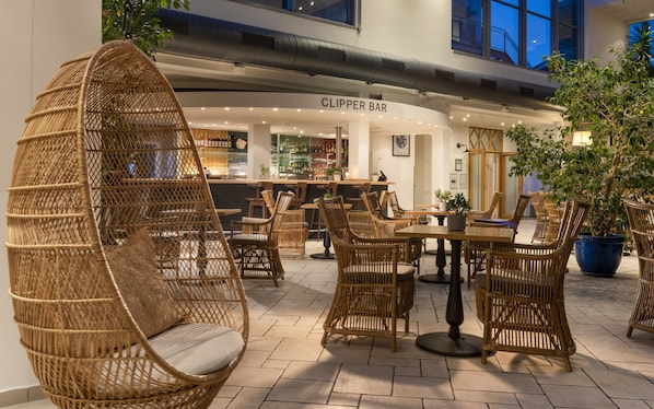 A wicker lounge area with tables and chairs, a bar named 'CLIPPER BAR', and potted plants. - Sunday Resort Marina Wolfsbruch (Rheinsberg)