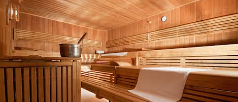 A sauna with wooden benches, a bench with a towel, and a metal bucket with a ladle.