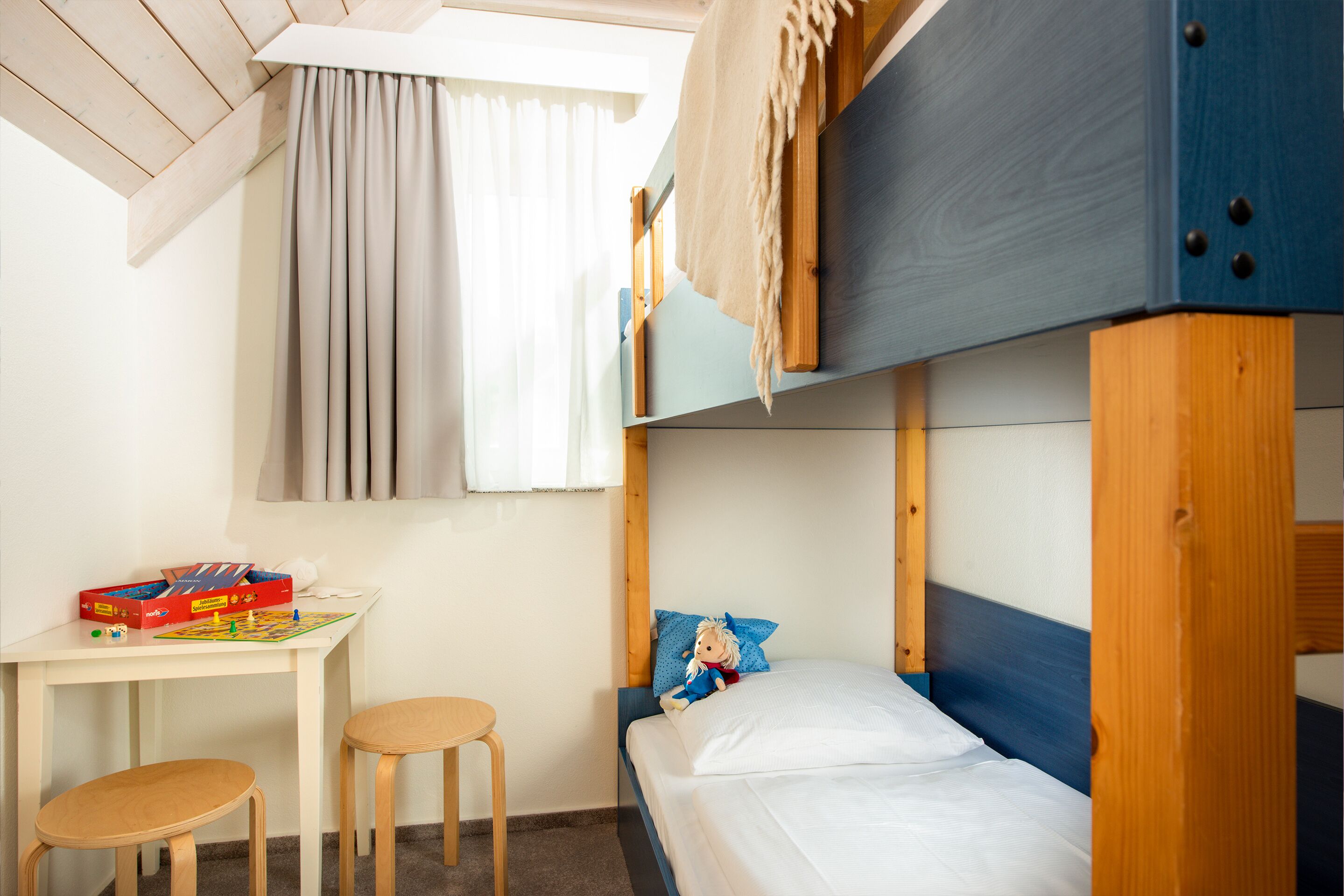 A bunk bed with a wooden headboard, a small table with a board game, and a chair.