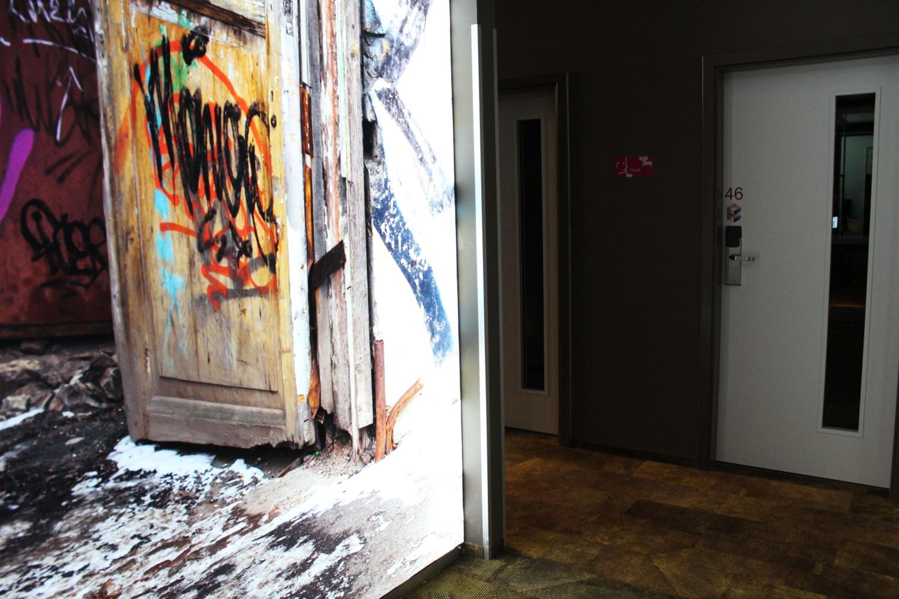 Un passadís amb una porta marcada amb el número 46, porta de fusta amb grafits i un sòl amb relleu.