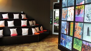 Un moderno vestíbulo de hotel con una zona de estar que incluye un sofá negro con cojines blancos y rojos, y una pared con arte callejero de colores.