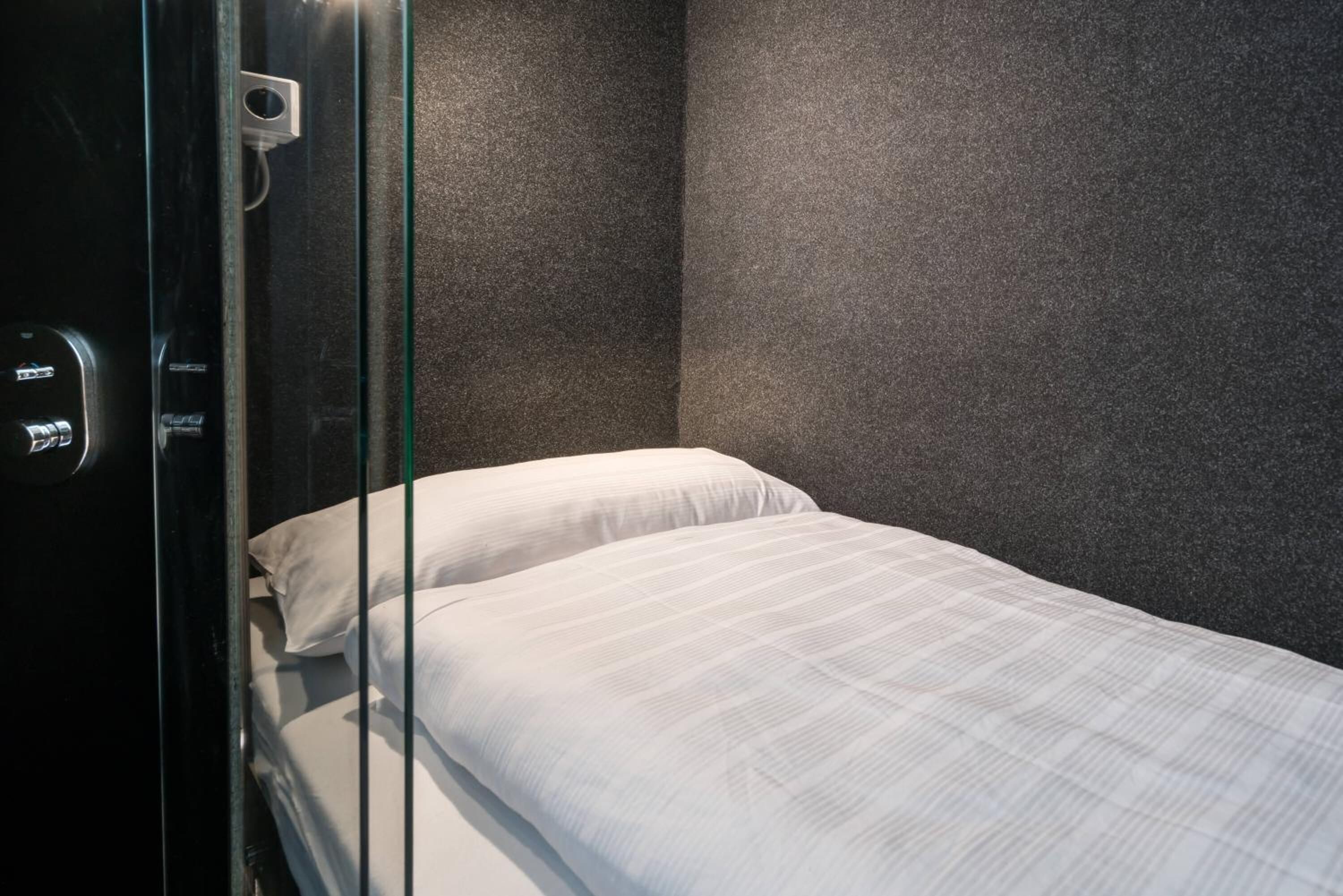 A hotel room with a bed, a glass door, and a control panel.