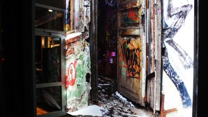 Un callejón con grafitis en paredes y puertas, piso de madera y entrada con puerta de cristal.