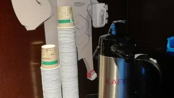 Una encimera de cocina con una cafetera, una pila de vasos desechables y un recorte de un personaje de dibujos animados.