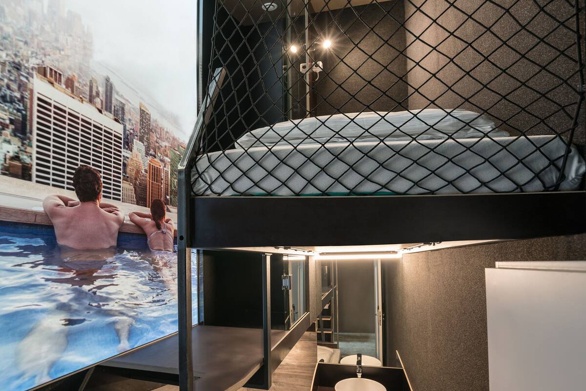 A bunk bed with a cityscape view, a small bathroom with a sink, and a pool area.