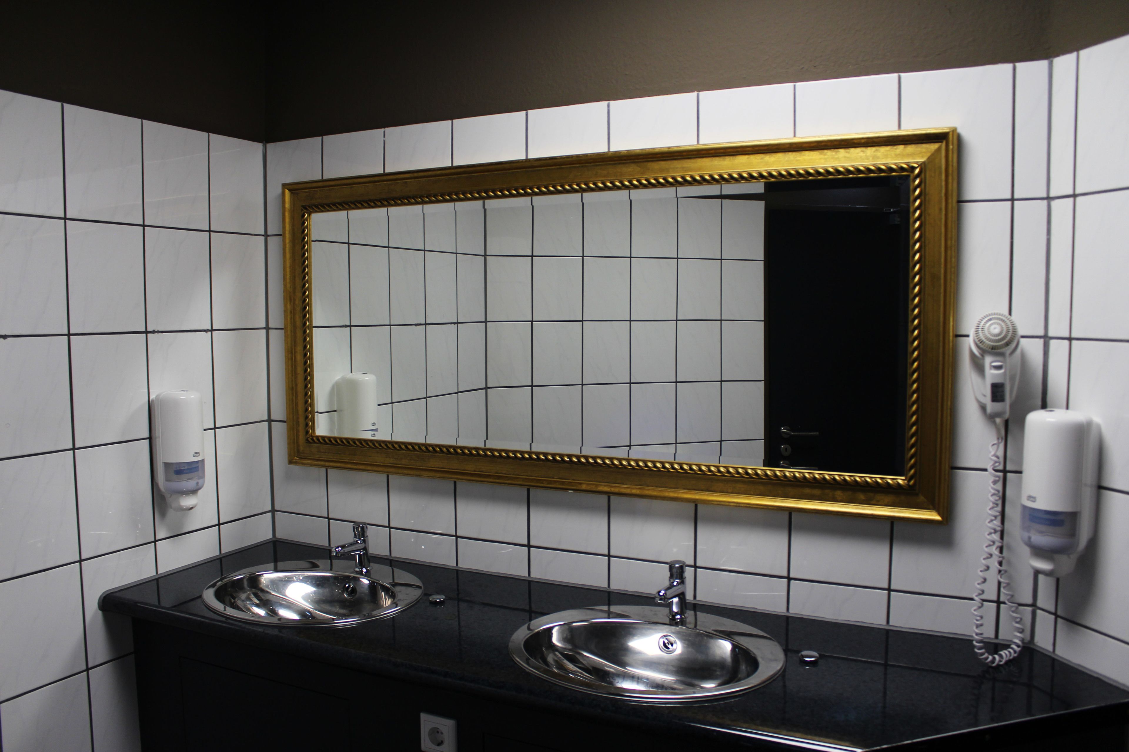Un baño con dos lavamanos, un espejo con marco dorado y un secador de pelo en la pared.