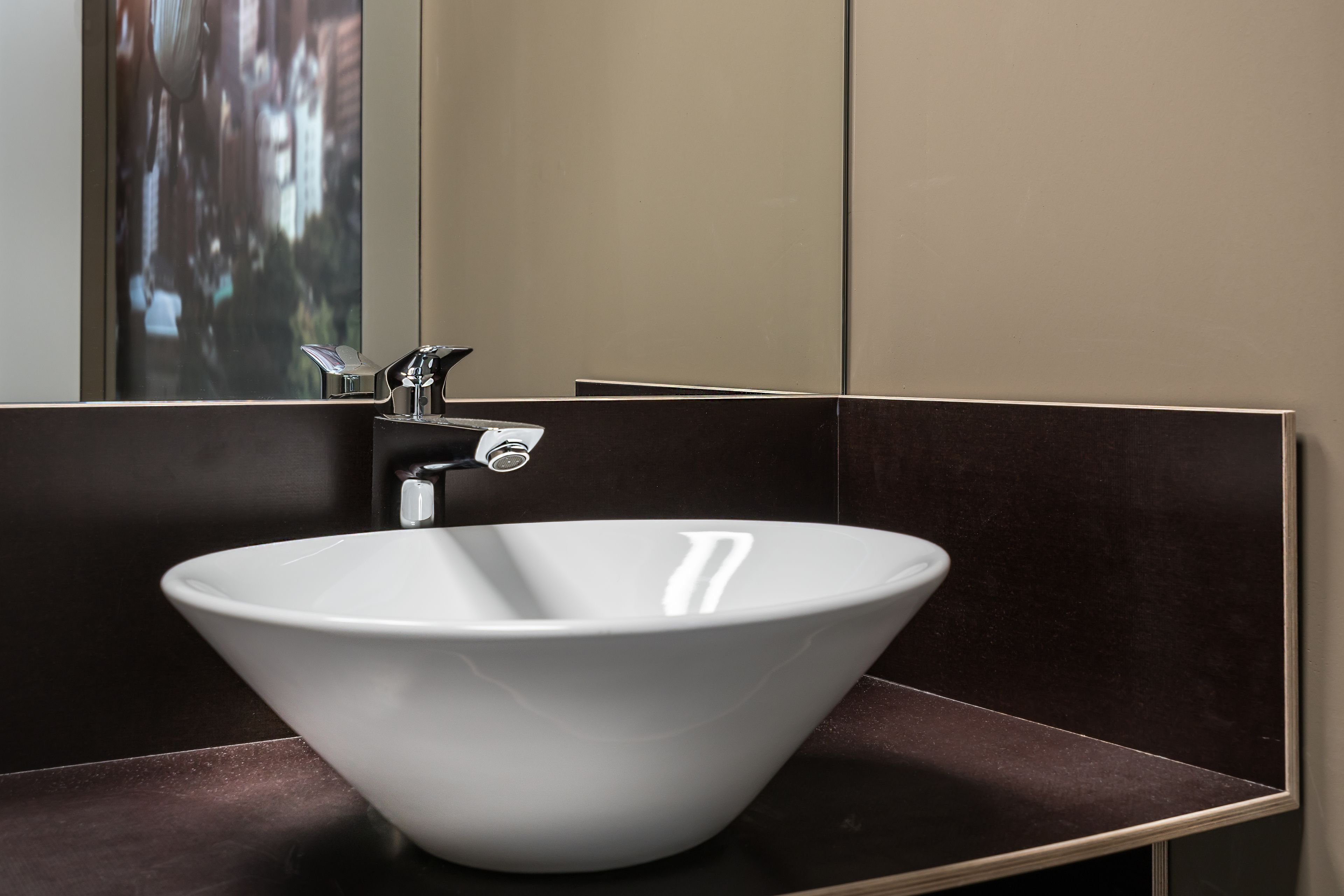 A modern bathroom with a white vessel sink, a mirror, and dark-toned walls.