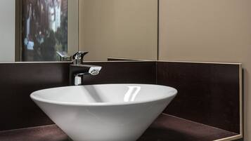 A modern bathroom with a white vessel sink, a mirror, and dark-toned walls.