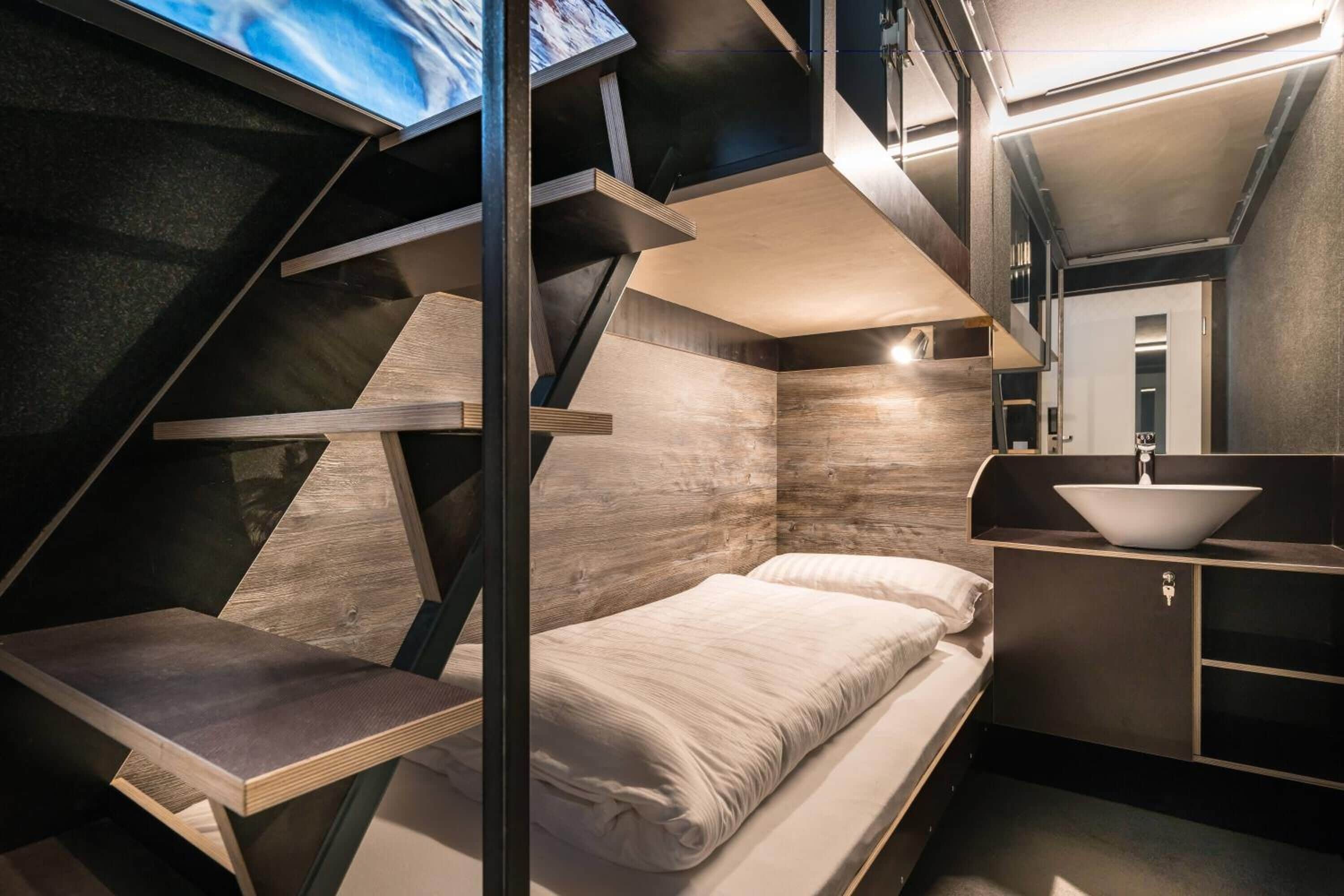 A modern, compact room with a bed, a small table, and a built-in sink.