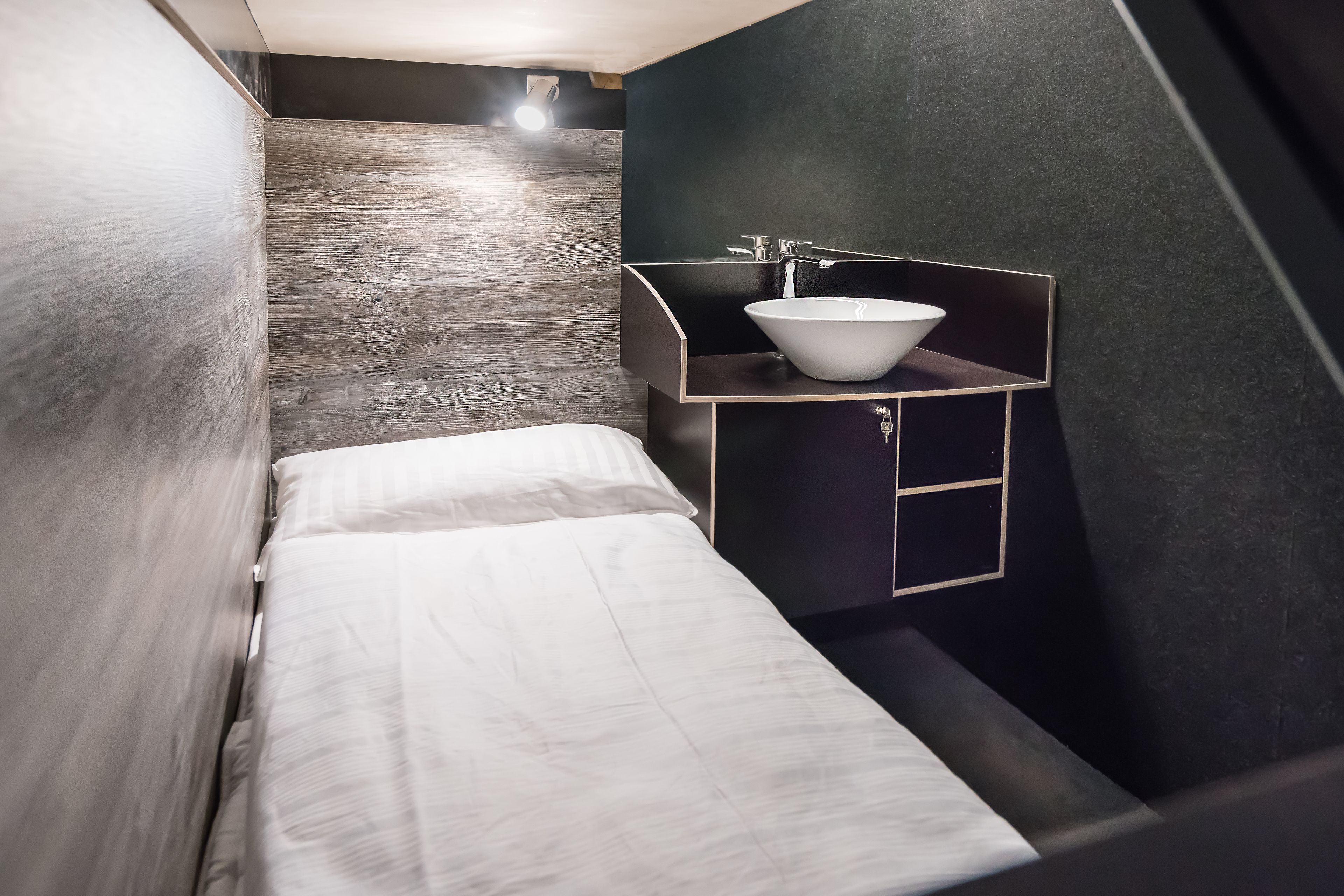 A compact, modern bathroom with a minimalist design, featuring a single white sink and a small bedside table.