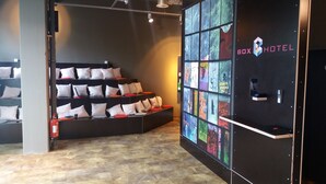 Un hall de hotel con zona de estar que incluye cojines blancos y rojos, una pared con arte de colores, y un letrero que dice "BOX HOTEL".