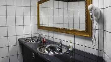 A bathroom with two sinks, a mirror with a gold frame, and a hairdryer mounted on the wall.