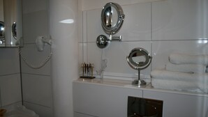 A bathroom with a toilet, a hairdryer, and three mirrors on the wall.