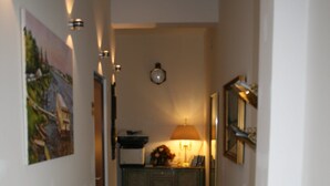 A hallway with a red carpet, a clock on the wall, and a vase with umbrellas.