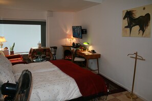 A hotel room with a bed, a desk, a chair, a lamp, a television, and a painting on the wall. - Das Hanse Quartier (Hamburg)