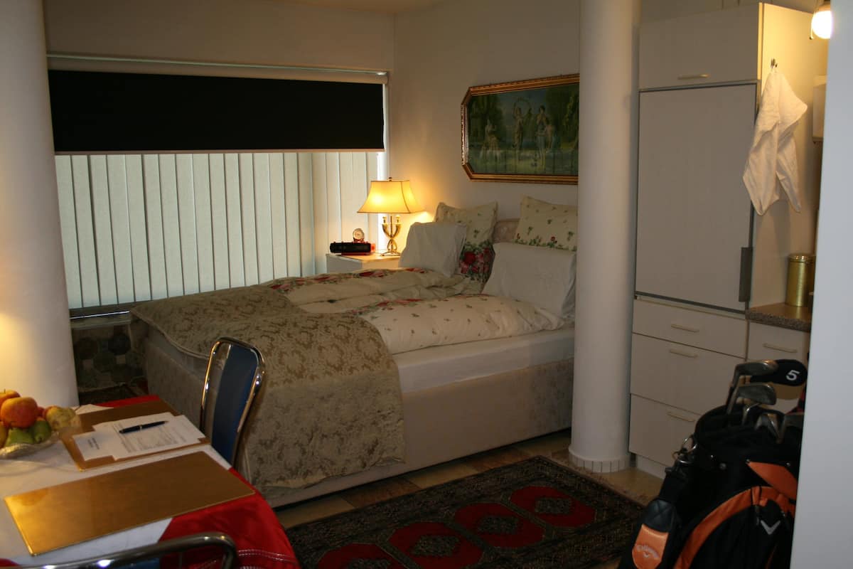 Ein kleines Hotelzimmer mit Bett, Nachttisch, Lampe und einem kleinen Schreibtisch mit Stuhl.