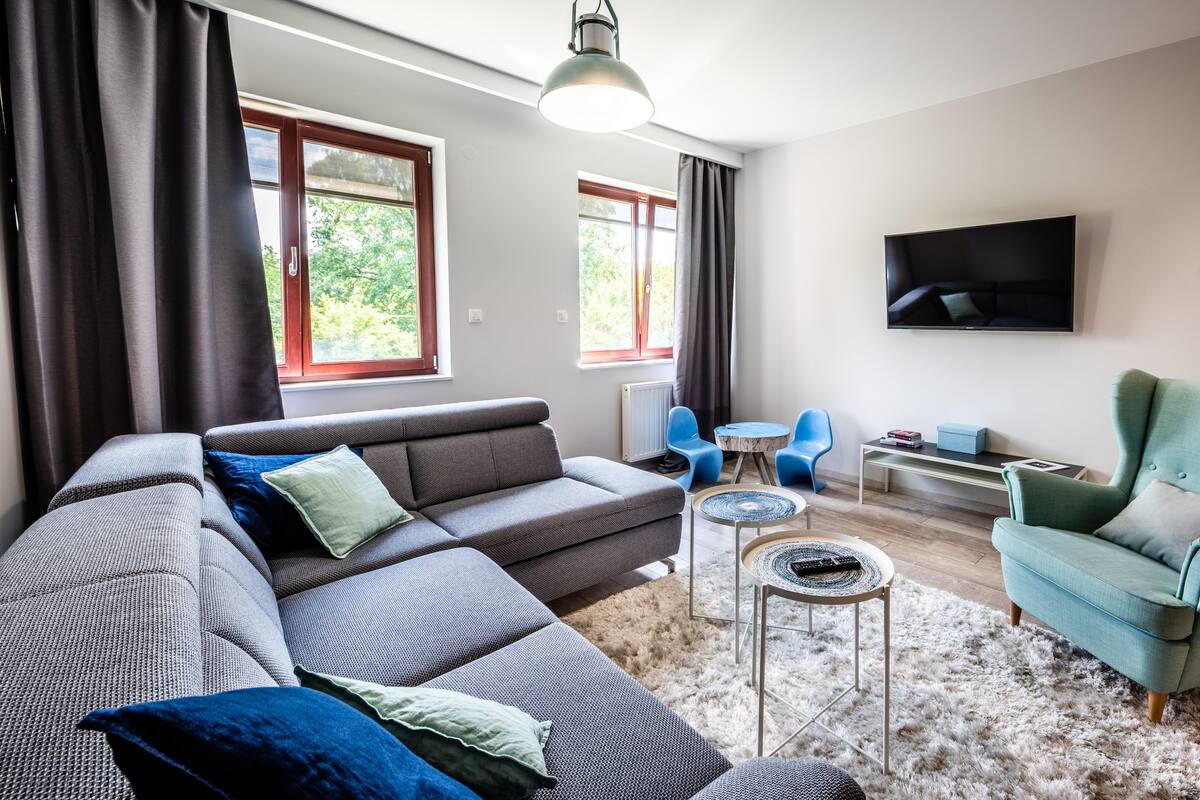 A modern living room with a grey sectional sofa, a teal armchair, and a flat-screen TV mounted on the wall.