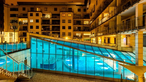 Ein modernes Hotel mit einem gläsernen Schwimmbad, mehreren Balkonen und einer gut beleuchteten Fassade.