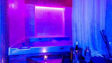 Een wellnessruimte met een jacuzzi, kaarsen en champagneflessen.