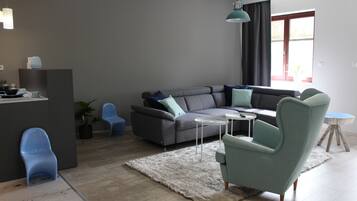 Uma sala de estar moderna com um sofá cinzento, cadeiras azuis, uma mesinha branca e um tapete branco.