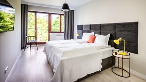 Ein modernes Schlafzimmer mit einem großen Bett, einer Nachttischlampe und Blick auf Grünfläche.